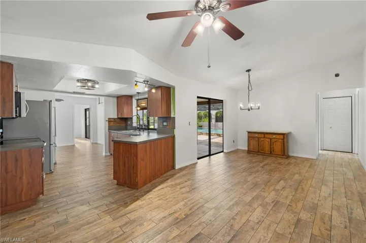 Kitchen featuring hardwood / wood-style flooring, ceiling fan with notable chandelier, pendant lighting, kitchen peninsula, and backsplash