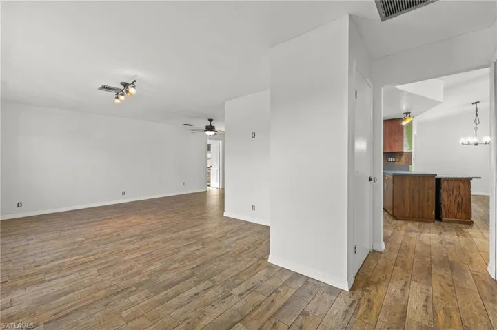 Spare room featuring ceiling fan with notable chandelier and wood-type flooring