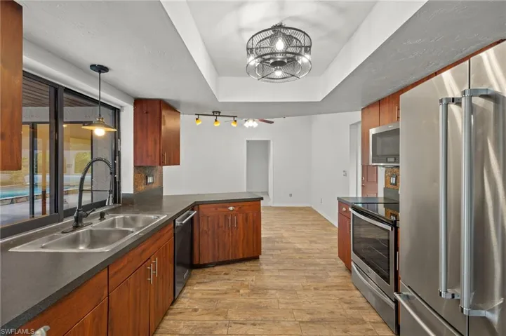 Kitchen with light wood-type flooring, a tray ceiling, hanging light fixtures, appliances with stainless steel finishes, and sink