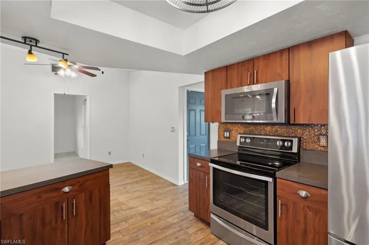 Kitchen featuring decorative backsplash, appliances with stainless steel finishes, light wood-type flooring, and ceiling fan