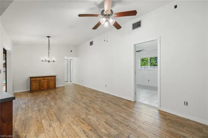 Unfurnished living room featuring ceiling fan with notable chandelier and light hardwood / wood-style floors