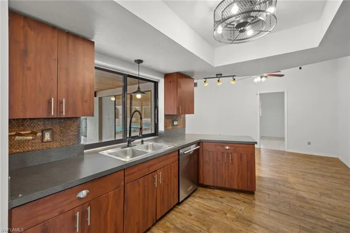 Kitchen featuring kitchen peninsula, dishwasher, ceiling fan, decorative backsplash, and a raised ceiling