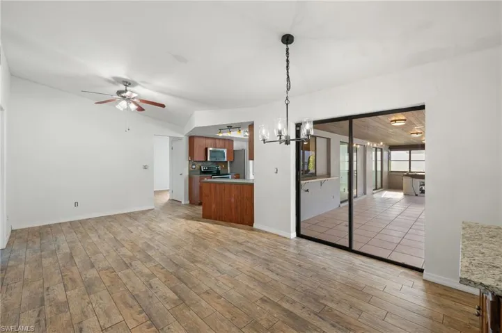 Unfurnished living room featuring hardwood / wood-style flooring, ceiling fan with notable chandelier, and lofted ceiling