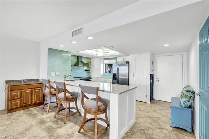 Kitchen with stainless steel fridge with ice dispenser, kitchen peninsula, ceiling fan, wall chimney exhaust hood, and a kitchen breakfast bar