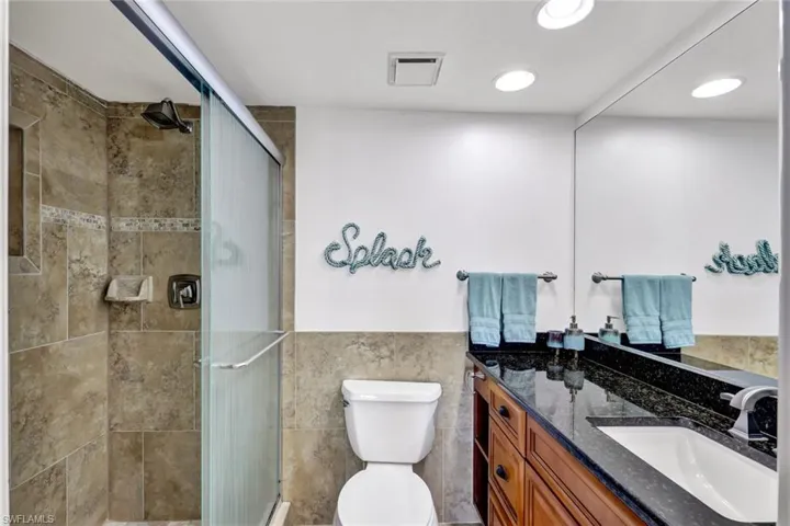 Bathroom featuring a shower with shower door, vanity, tile walls, and toilet