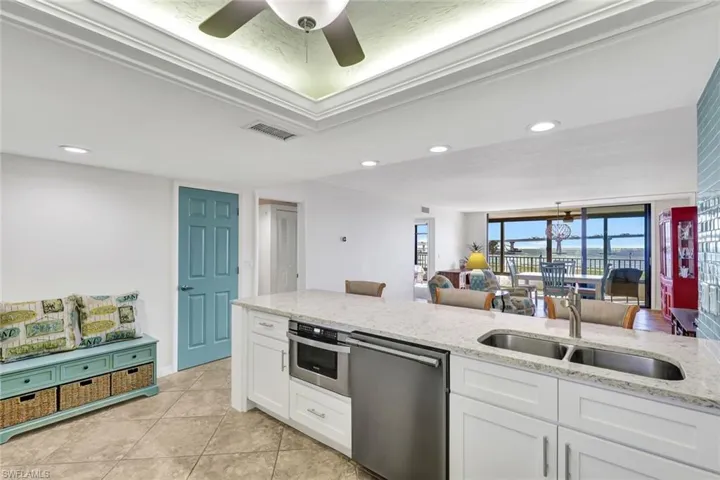 Kitchen with white cabinetry, ceiling fan, stainless steel appliances, sink, and light stone counters