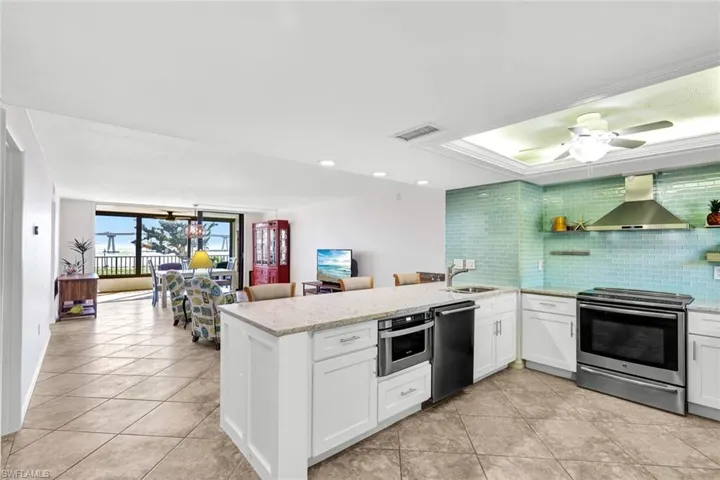 Kitchen featuring appliances with stainless steel finishes, white cabinets, wall chimney range hood, backsplash, and ceiling fan