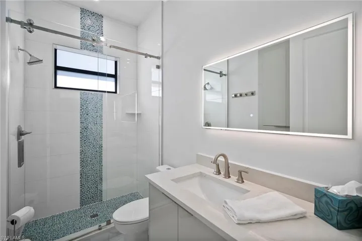 Bathroom featuring a shower with door, toilet, and vanity