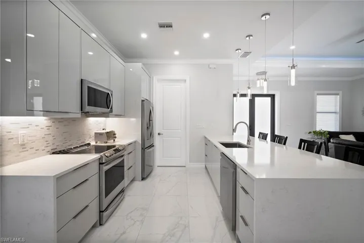 Kitchen featuring tasteful backsplash, hanging light fixtures, sink, a kitchen island with sink, and appliances with stainless steel finishes
