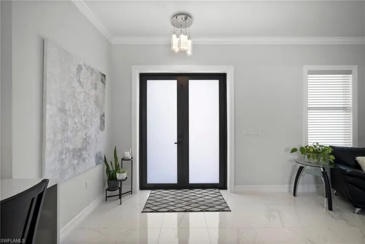 Entryway featuring an inviting chandelier, ornamental molding, light tile flooring, and french doors