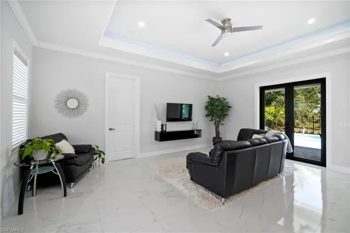 Tiled living room with ceiling fan, a tray ceiling, crown molding, and french doors