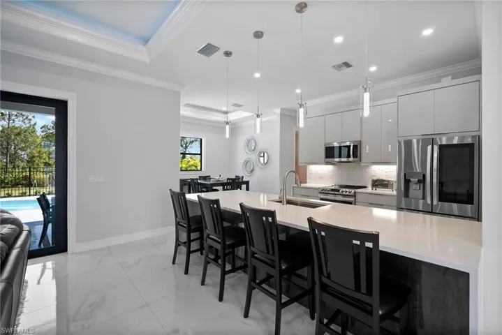 Kitchen with appliances with stainless steel finishes, an island with sink, pendant lighting, sink, and a raised ceiling