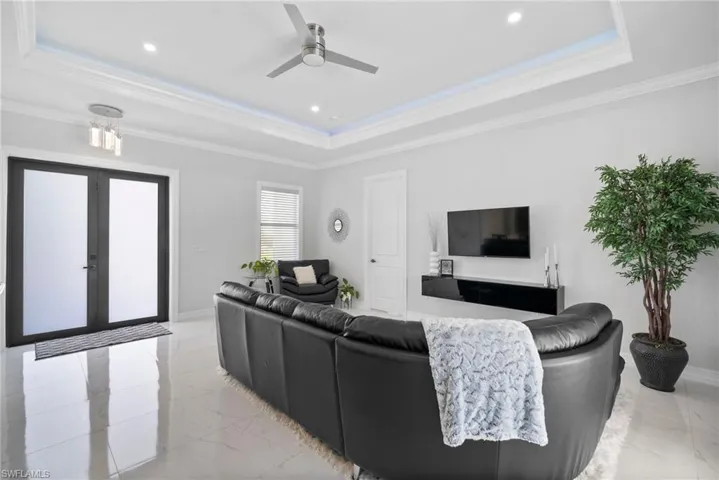 Living room featuring crown molding, french doors, a tray ceiling, ceiling fan, and light tile floors