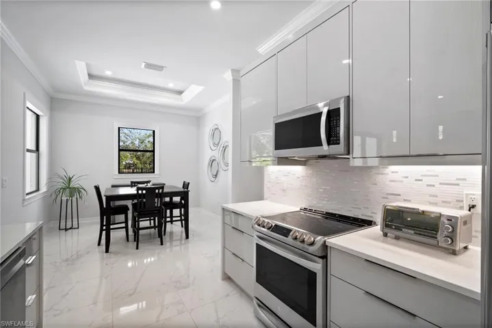Kitchen with backsplash, a tray ceiling, crown molding, appliances with stainless steel finishes, and light tile floors