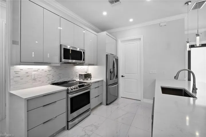 Kitchen featuring backsplash, crown molding, appliances with stainless steel finishes, sink, and pendant lighting