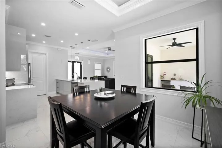 Tiled dining space with crown molding, sink, ceiling fan, and a raised ceiling
