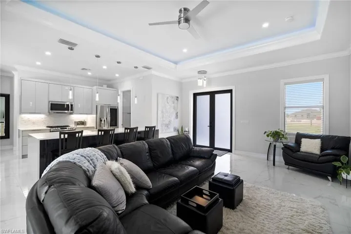 Living room with a tray ceiling, ornamental molding, ceiling fan, and light tile floors
