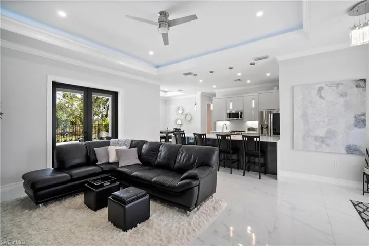 Living room with crown molding, french doors, a tray ceiling, ceiling fan, and light tile floors