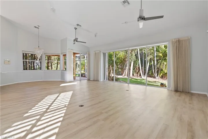 Unfurnished living room with light wood-type flooring, ceiling fan, a chandelier, and high vaulted ceiling