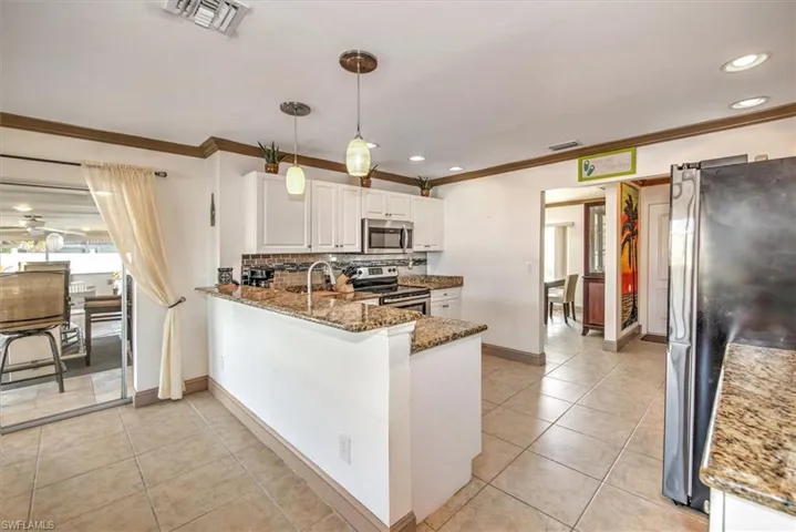 Kitchen with appliances with stainless steel finishes, dark stone countertops, white cabinets, crown molding, and decorative light fixtures