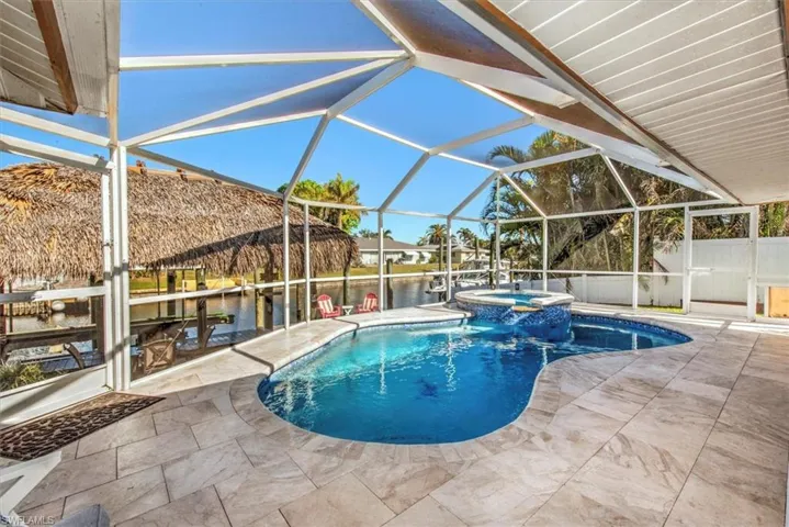 View of swimming pool featuring glass enclosure, a sunroom, a pool with connected hot tub, a patio, and a water view
