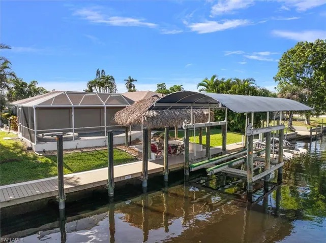 Dock area with boat lift, glass enclosure, a water view, a sunroom, and a lawn
