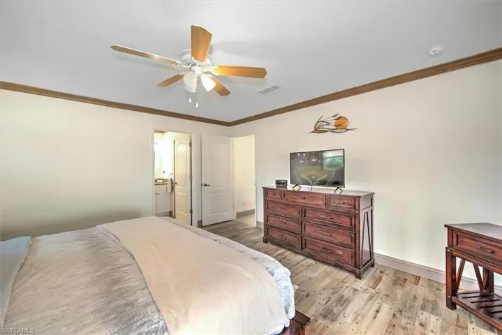 Bedroom featuring a ceiling fan, light wood finished floors, ornamental molding, and connected bathroom