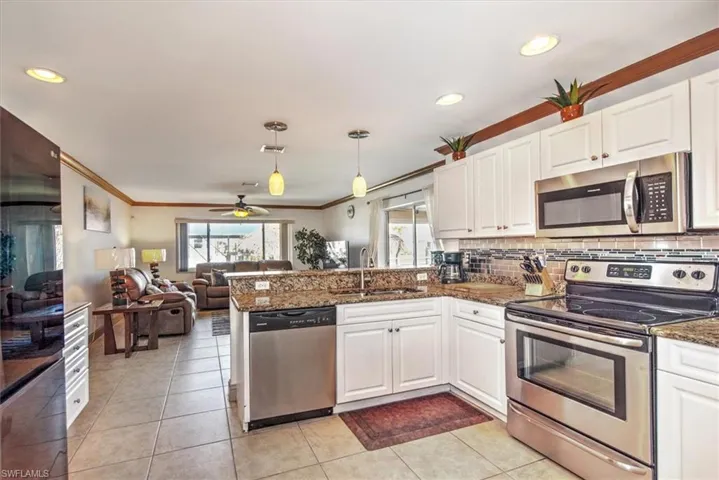 Kitchen with stainless steel appliances, white cabinetry, dark stone countertops, a peninsula, and ornamental molding