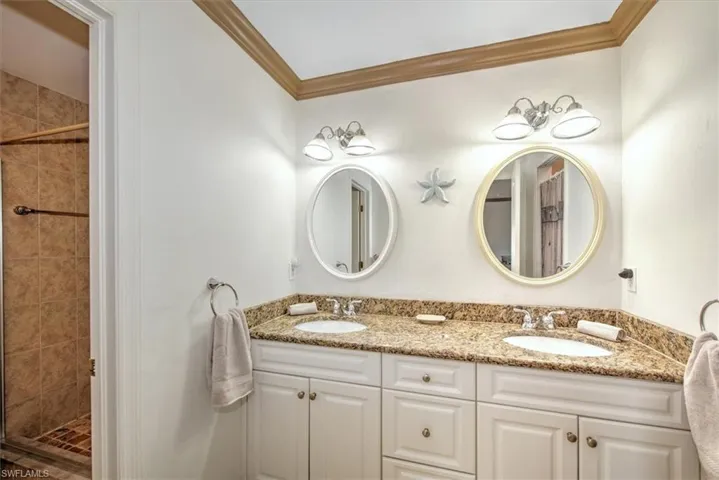 Bathroom with double vanity, a shower stall, and ornamental molding