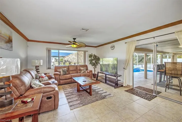 Living area with ceiling fan, light tile patterned floors, and crown molding