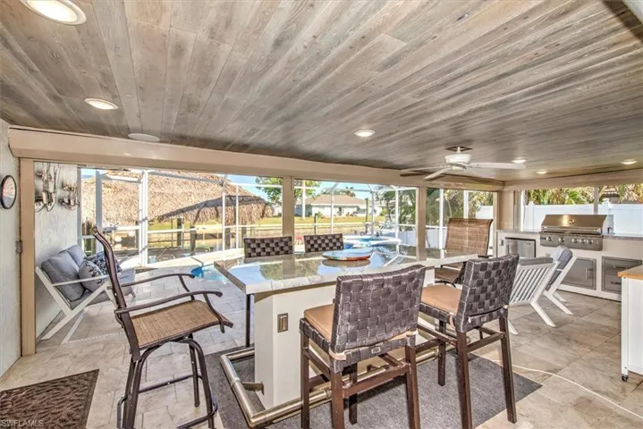 View of patio featuring an outdoor kitchen, ceiling fan, glass enclosure, and wine cooler