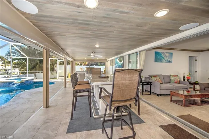 View of patio / terrace featuring an outdoor kitchen, ceiling fan, a pool with connected hot tub, a sunroom, and glass enclosure