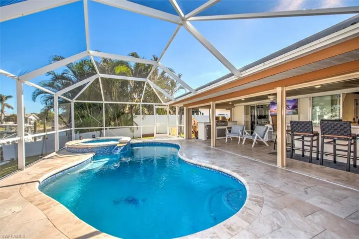 View of swimming pool featuring a lanai, a pool with connected hot tub, a sunroom, a patio, and an outdoor kitchen