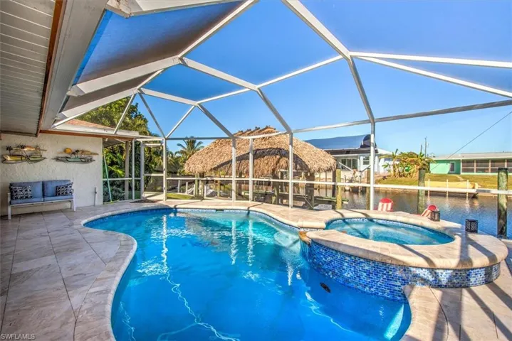 View of pool with a sunroom, a pool with connected hot tub, a patio area, glass enclosure, and a water view
