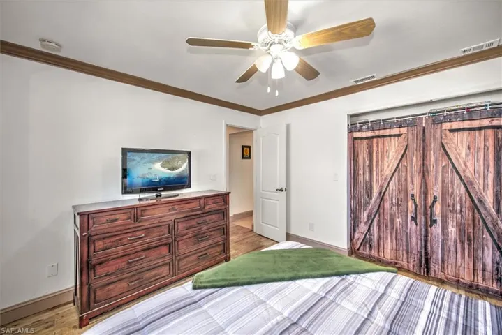 Bedroom featuring ornamental molding, ceiling fan, light wood-type flooring, and a barn door