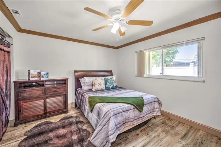 Bedroom with ornamental molding, a barn door, ceiling fan, and wood finished floors