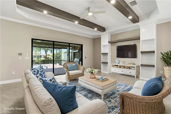 Virtually Staged. Unfurnished living area with custom ceiling beams, crown molding, tray ceilings, ceiling fan w/ light and controls, floor plug, custom built-in entertainment center, custom remote slider blinds, recessed lighting, and light tile patterned floors