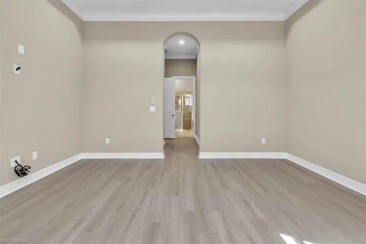 Empty room with arched walkways, light wood-type flooring, and crown molding