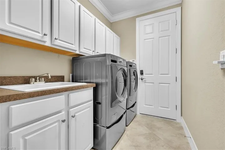Laundry area featuring crown molding, washer and clothes dryer, cabinet space, and light tile patterned floors