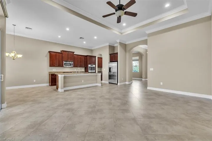 Kitchen featuring open floor plan, arched walkways, a ceiling fan, a center island with sink, and crown molding
