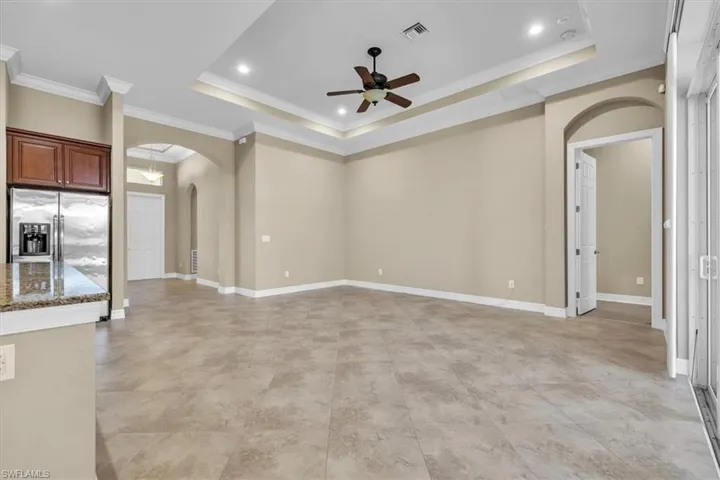 Unfurnished living room with arched walkways, a ceiling fan, crown molding, a tray ceiling, and recessed lighting