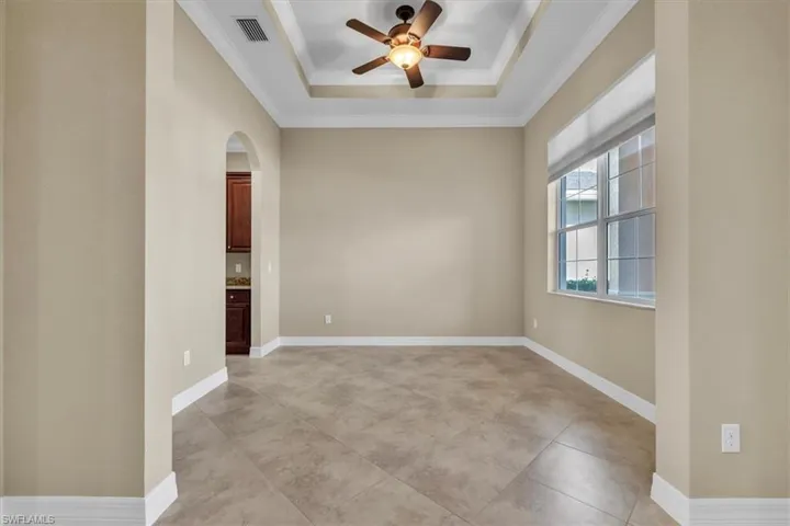 Unfurnished room with arched walkways, crown molding, a ceiling fan, a tray ceiling, and light tile patterned flooring