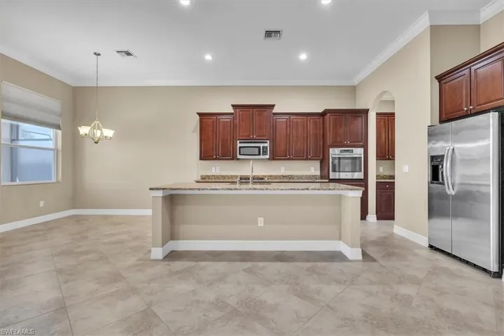 Kitchen featuring stainless steel appliances, ornamental molding, arched walkways, a kitchen island with sink, and light stone countertops