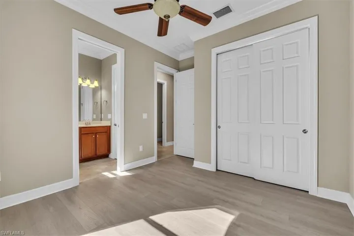 Unfurnished bedroom with light wood-style floors, crown molding, ceiling fan, a closet, and ensuite bathroom