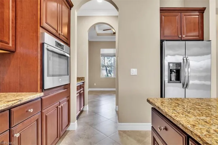 Kitchen with stainless steel appliances, ornamental molding, light stone counters, wood finish cabinets, and arched walkways