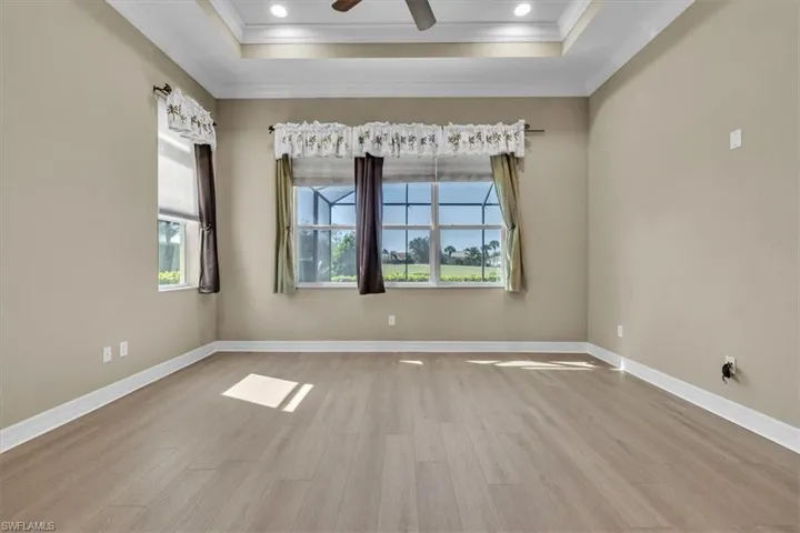 Spare room featuring a ceiling fan, light wood-type flooring, crown molding, and a tray ceiling
