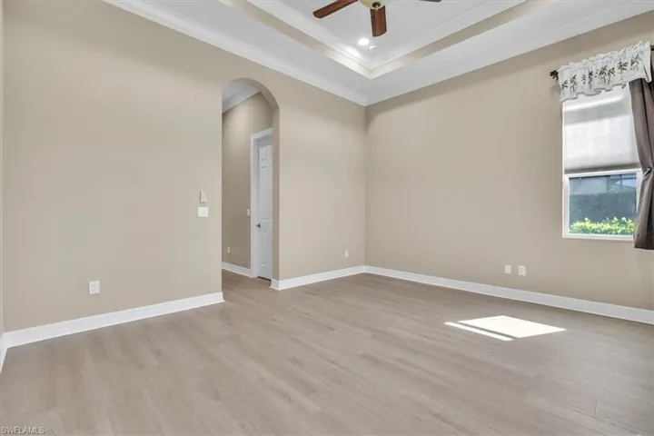 Empty room featuring ceiling fan, arched walkways, light wood-type flooring, crown molding, and a tray ceiling