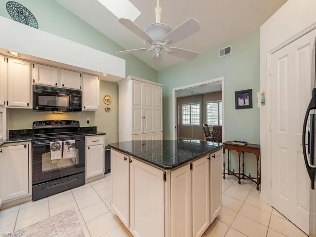 Kitchen with vaulted ceiling, dark stone counters, island, and pantry towards dining area