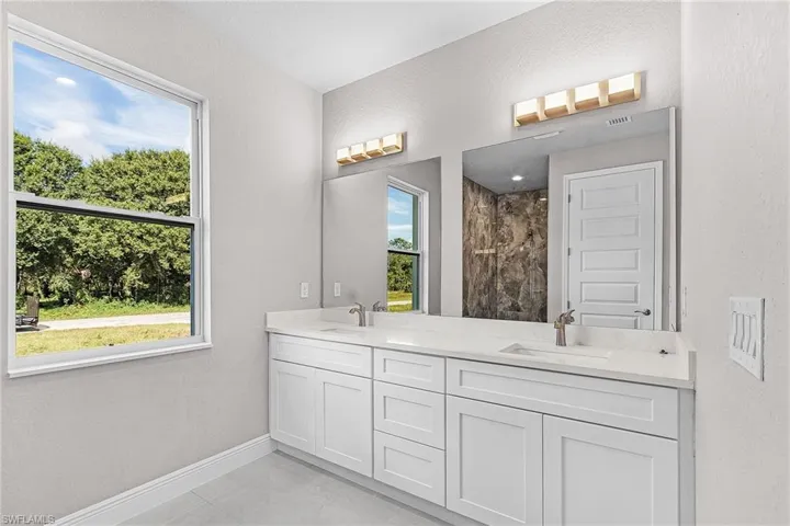 Full bath with tiled shower, double vanity, a textured wall, and tile patterned floors