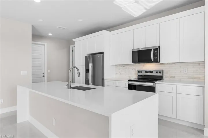 Kitchen featuring appliances with stainless steel finishes, an island with sink, white cabinetry, recessed lighting, and decorative backsplash